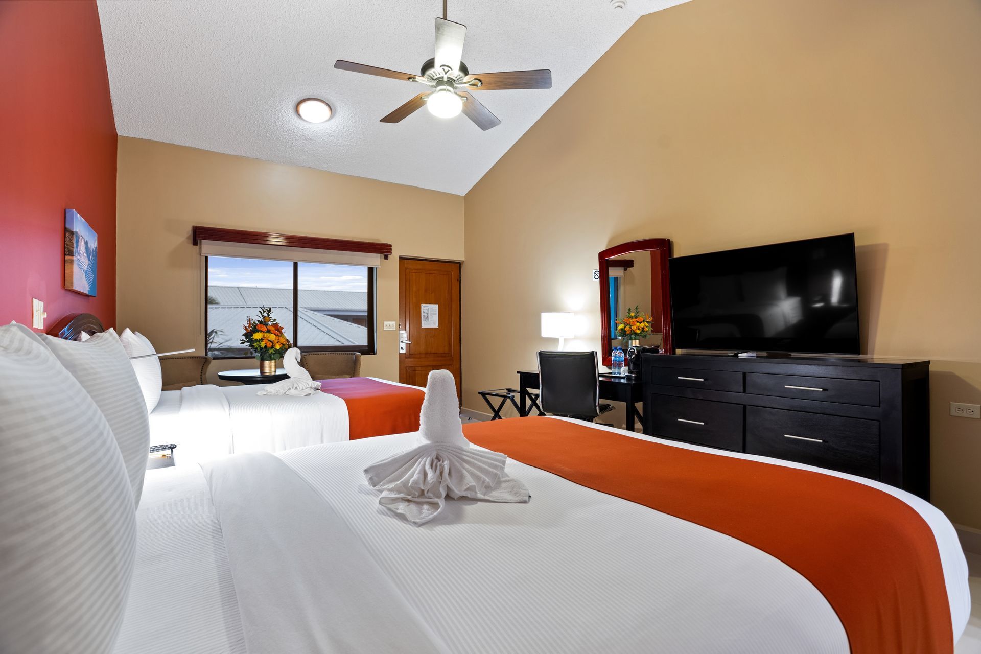 A hotel room with two beds , a television and a ceiling fan.