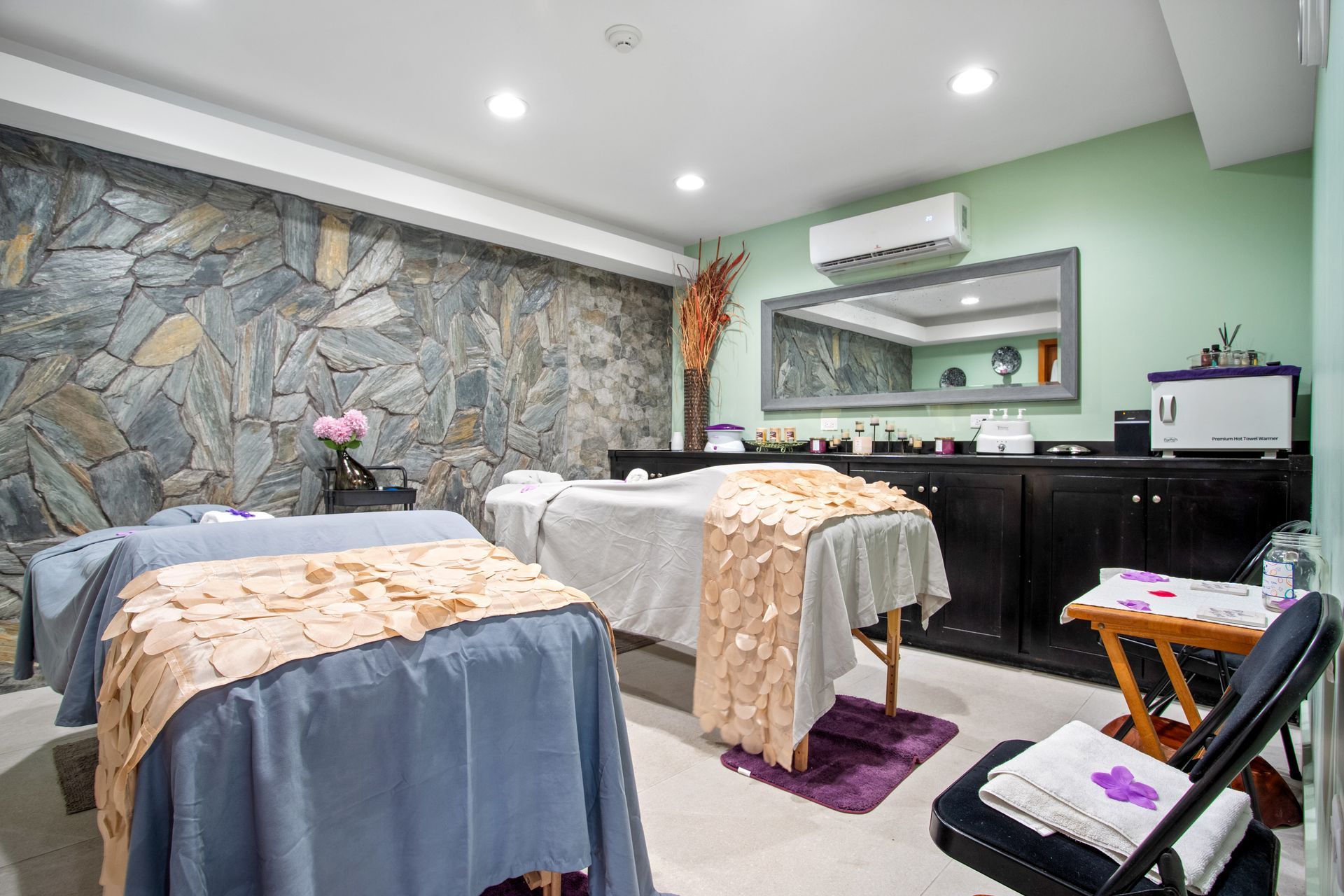 Two massage tables are in a room with a stone wall.