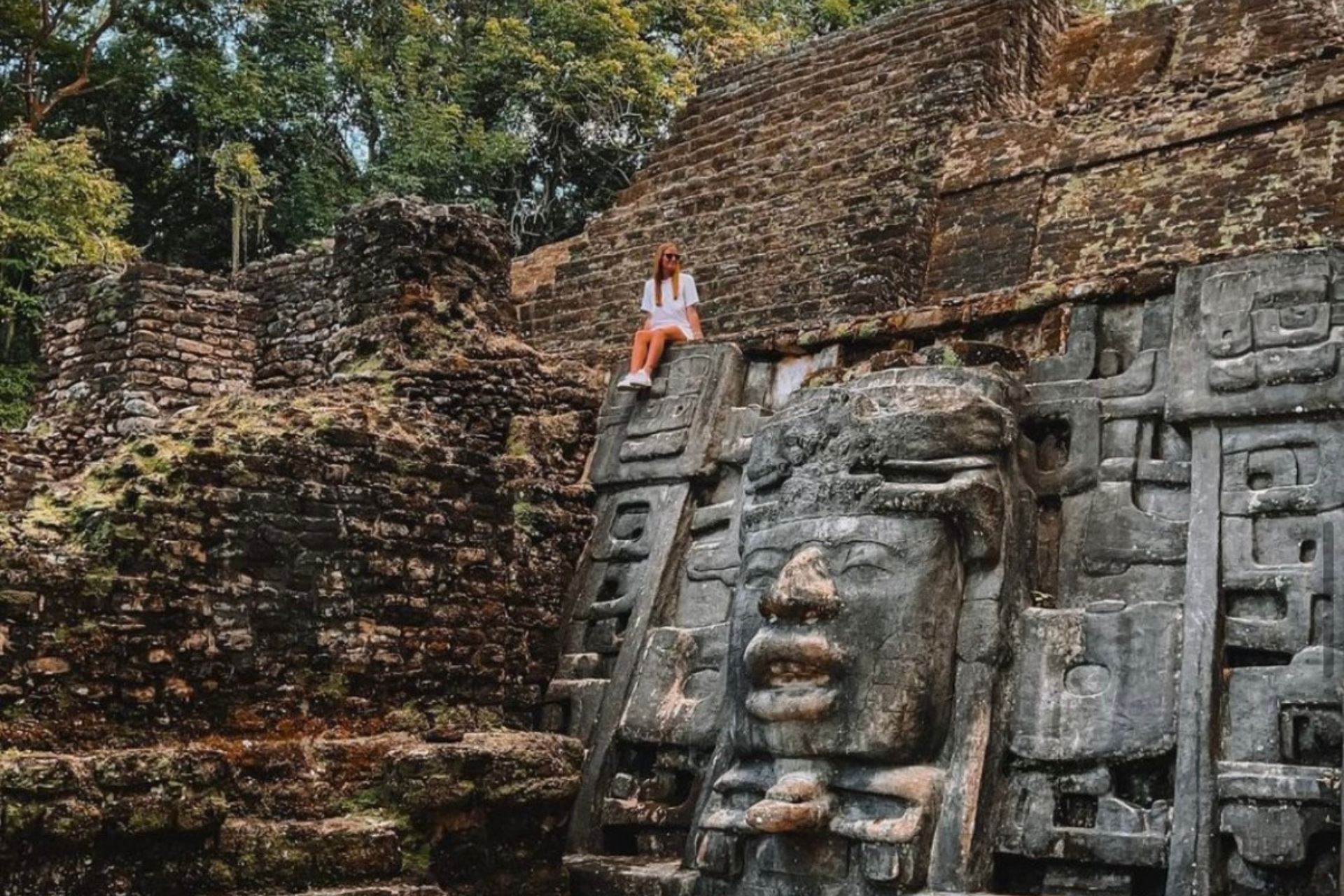 a woman is sitting on top of a large stone statue of a face .