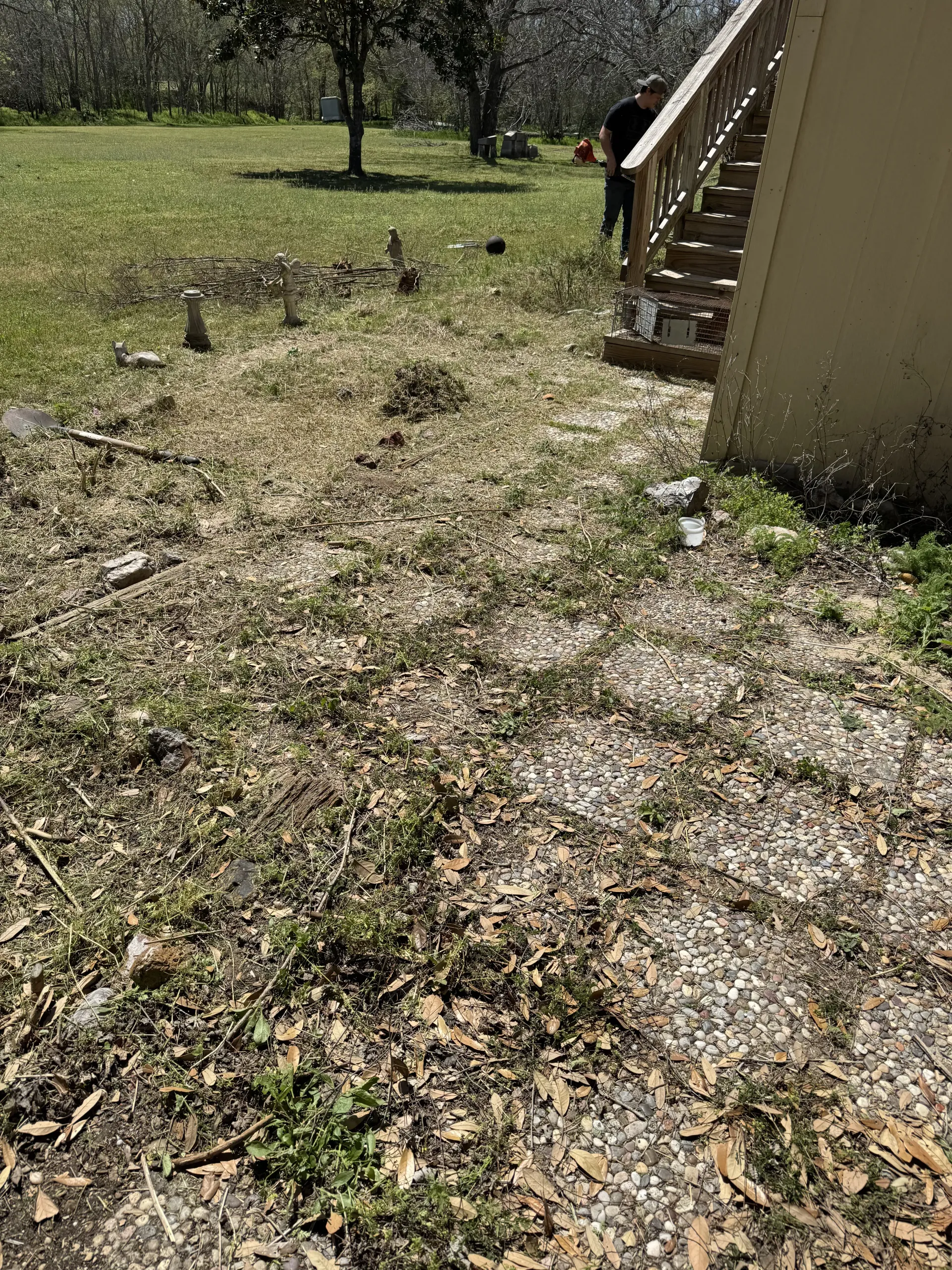 A person stands near outdoor wooden stairs next to a lawn covered in fallen leaves and debris.