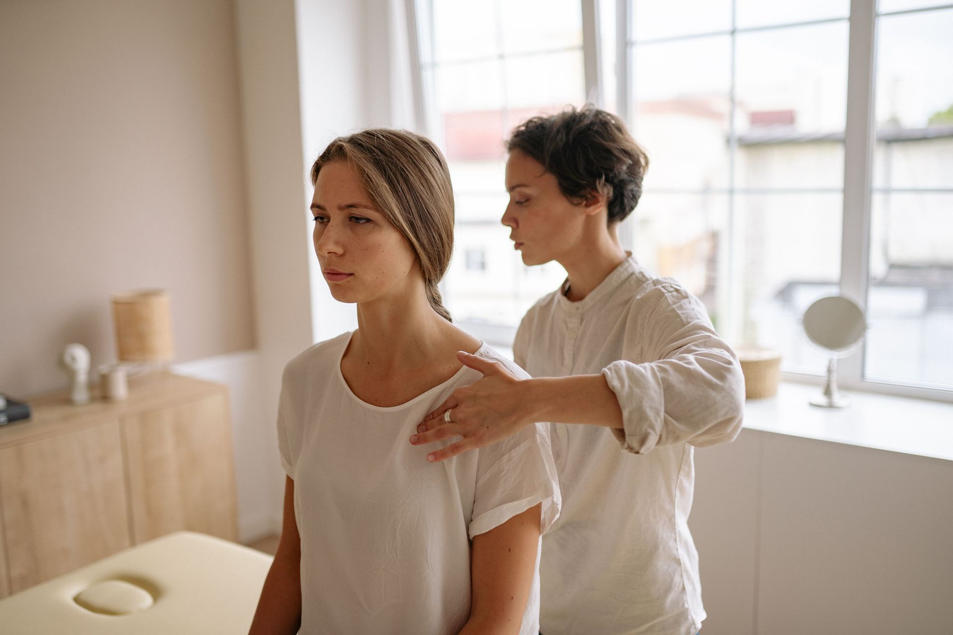 Physical therapist assessing a seated patient’s shoulder in a bright clinic room