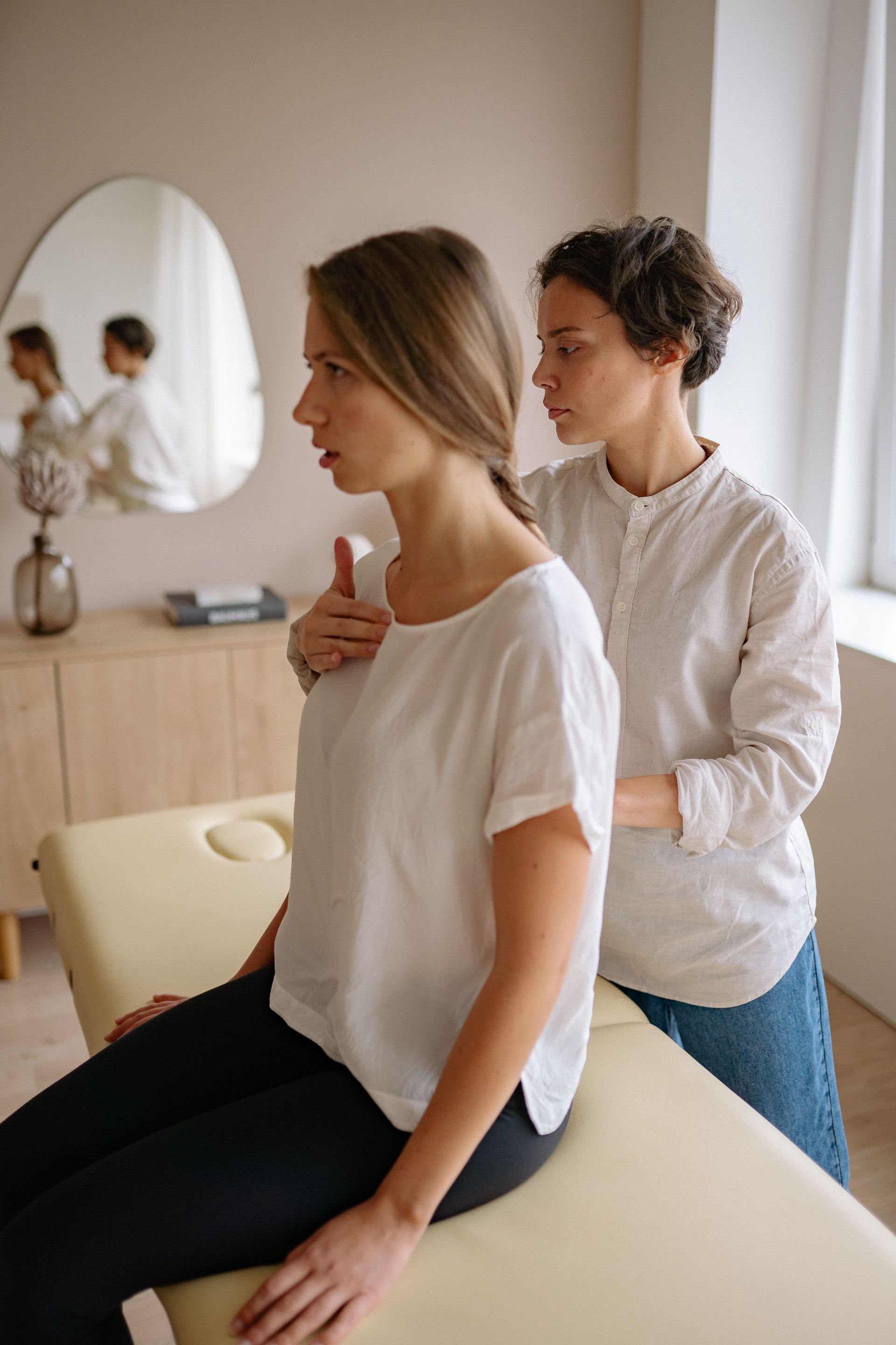 Physical therapist helping a seated client stretch in a bright clinic room