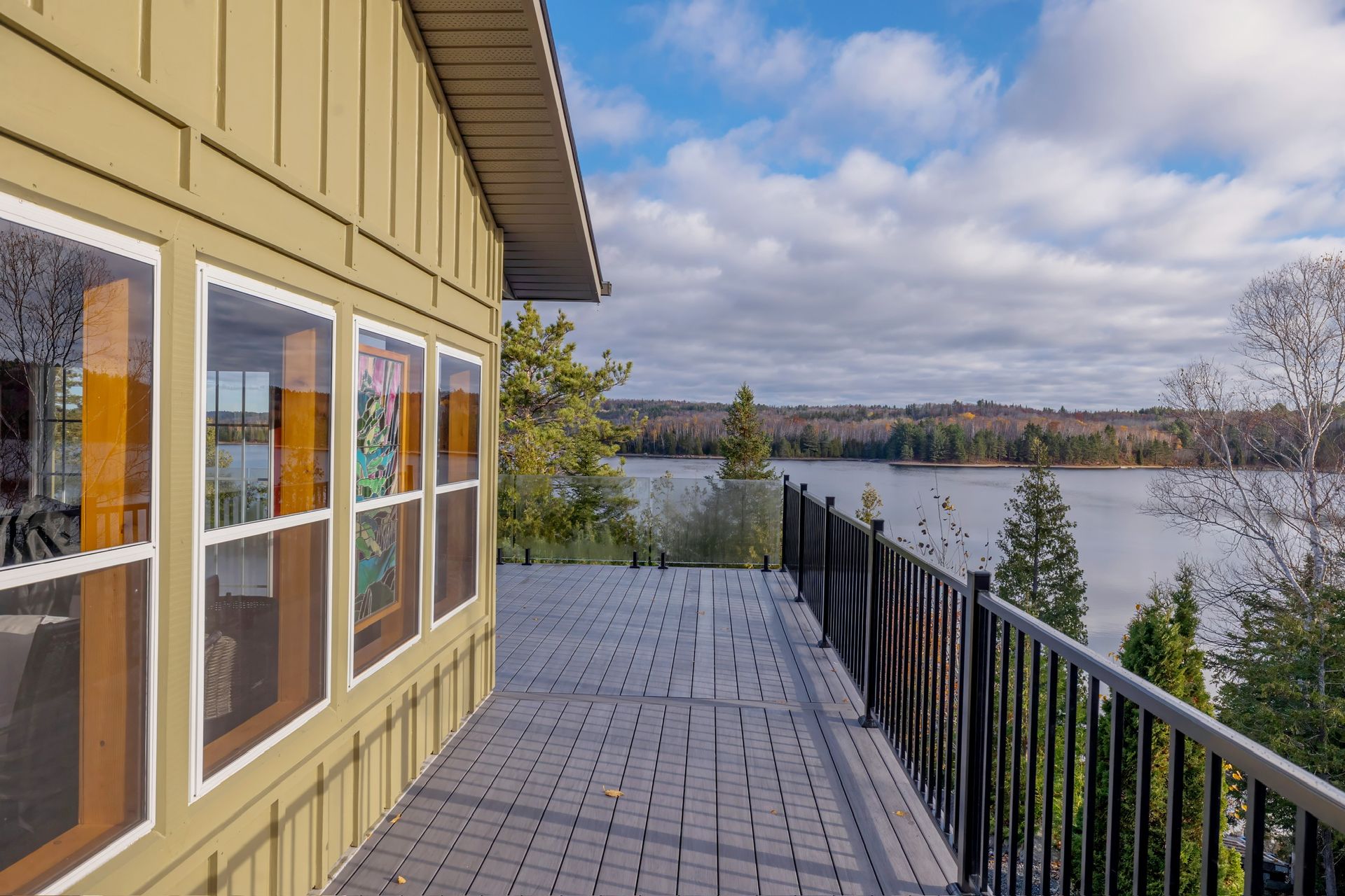 Wooden deck beside a yellow house overlooking a calm lake under a cloudy sky