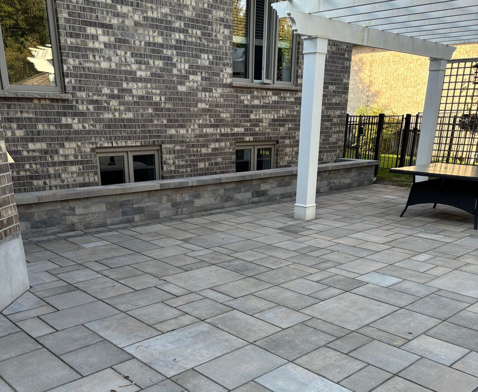 A patio with a pergola and chairs in front of a brick building.