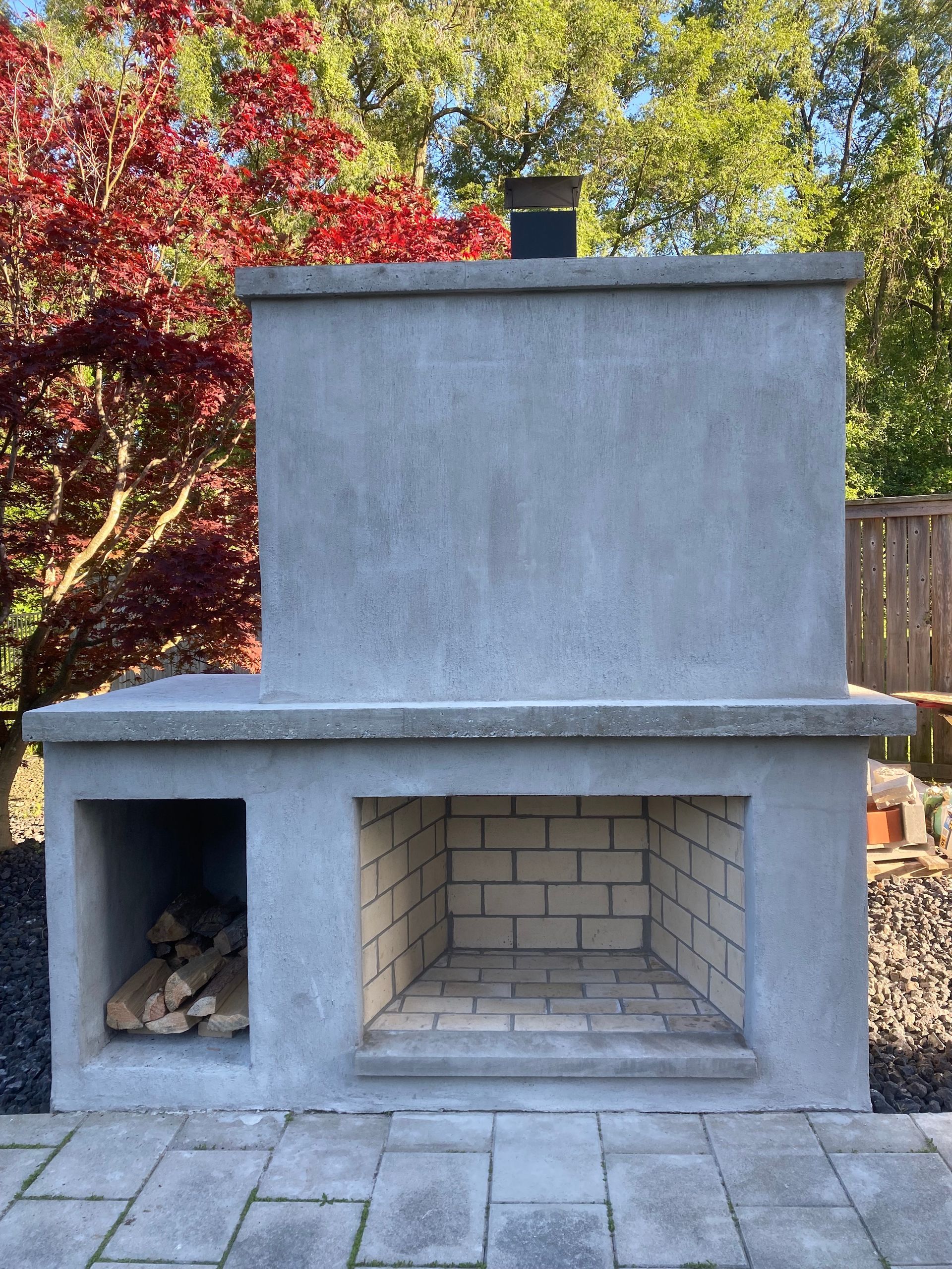 A brick fireplace is sitting on a brick patio next to a tree.