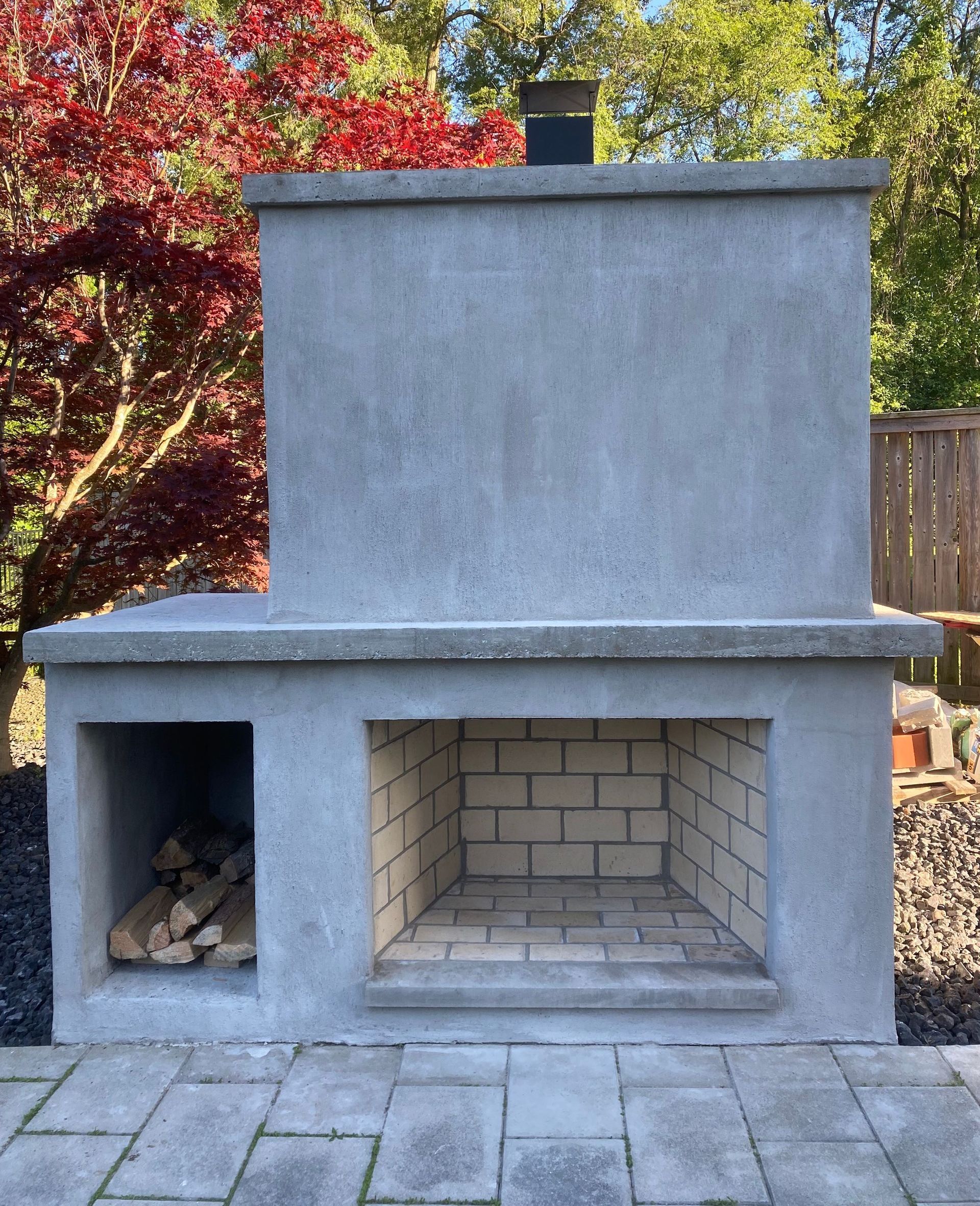 A brick fireplace is sitting on a brick patio next to a tree.