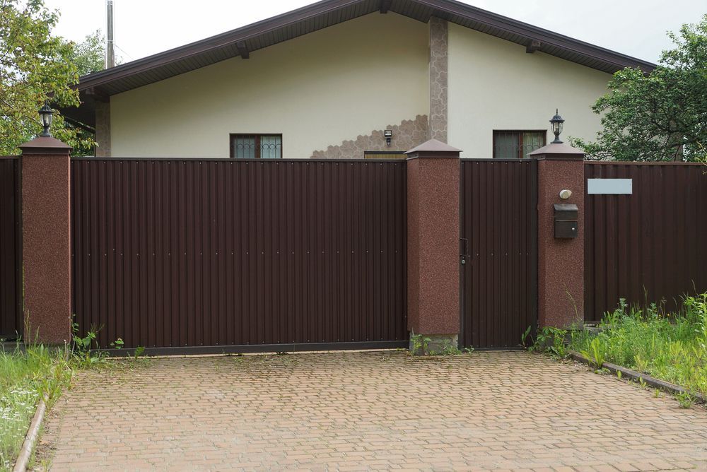 Brown metal gate and fence in front of a house with a cobblestone driveway
