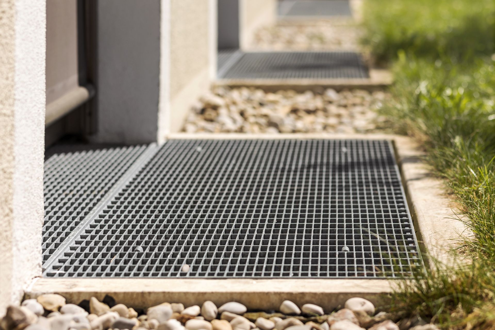 A close up of a metal grate on a sidewalk next to a house.