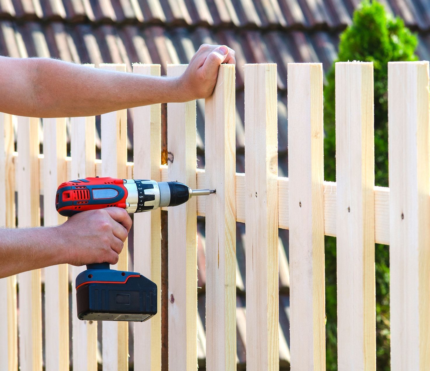 A person is using a drill to install a wooden fence.