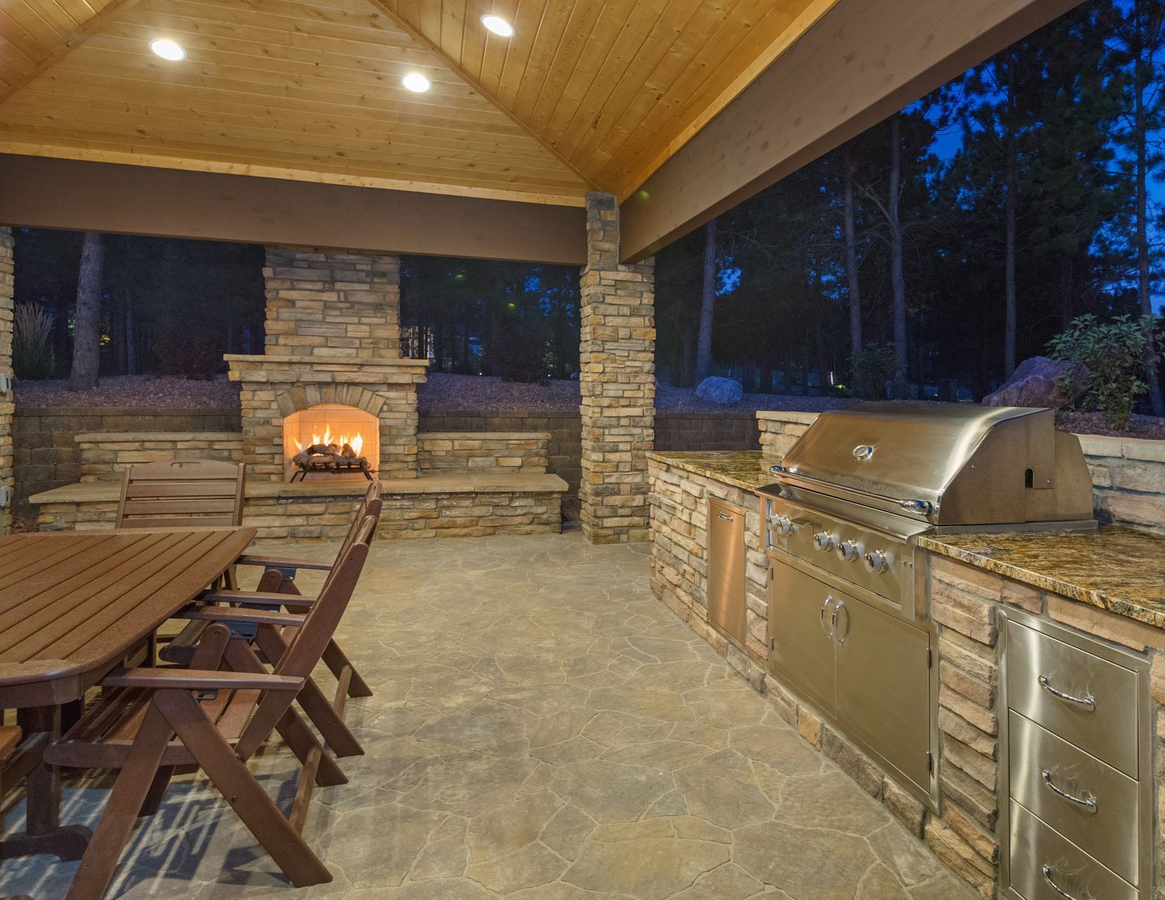 A large outdoor kitchen with a table and chairs and a fireplace.