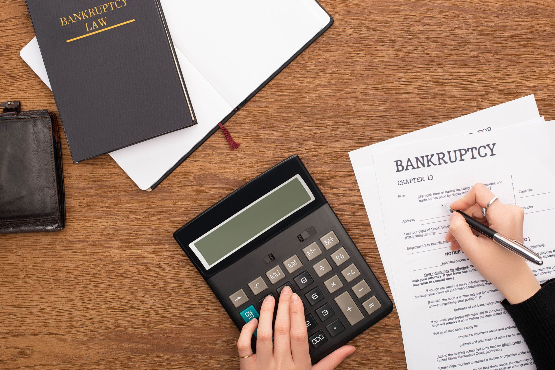 Hands using calculator while filling out Chapter 13 bankruptcy paperwork on a desk.