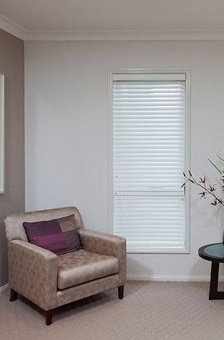 A Living Room with A Chair, Table and Window with Blinds — Creative Curtains & Blinds In Tweed Heads South, NSW