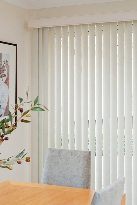 A Dining Room with A Wooden Table and Chairs and White Vertical Blinds — Creative Curtains & Blinds In Tweed Heads South, NSW