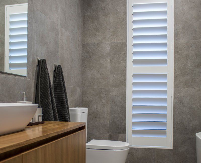 A Bathroom with A Toilet, Sink, Mirror and Shutters — Creative Curtains & Blinds In Tweed Heads South, NSW