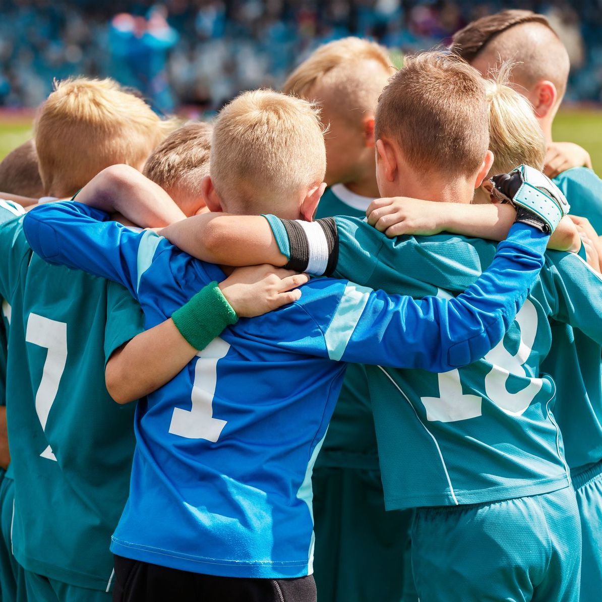 A group of young boys are hugging each other in a huddle and one of the boys has the number 11 on his back