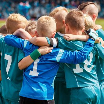 A group of young boys are hugging each other in a huddle and one of the boys has the number 11 on his back