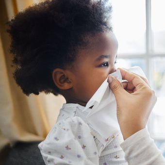 A little girl is blowing her nose with a tissue.