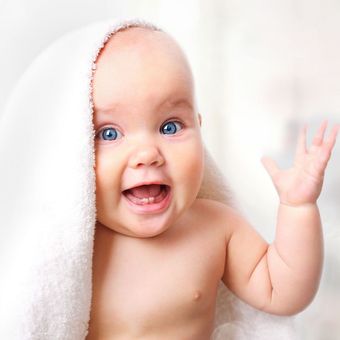 A baby is wrapped in a white towel and smiling.