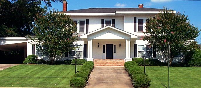 Large white two-story house with a front porch, brick steps, and a manicured lawn