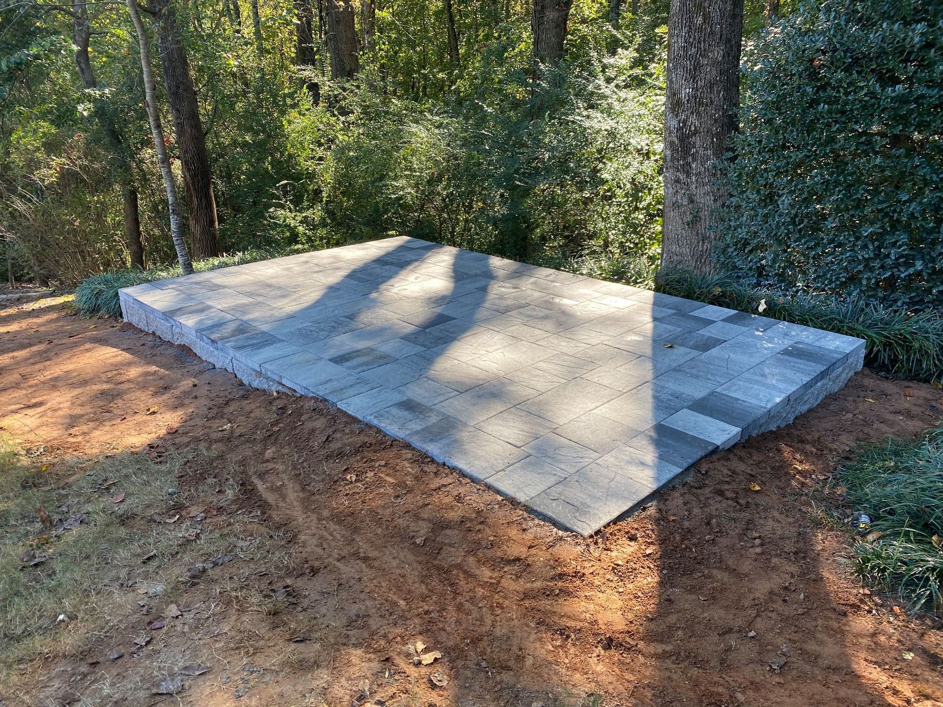 Concrete slab foundation in a wooded yard with sunlight and tree shadows