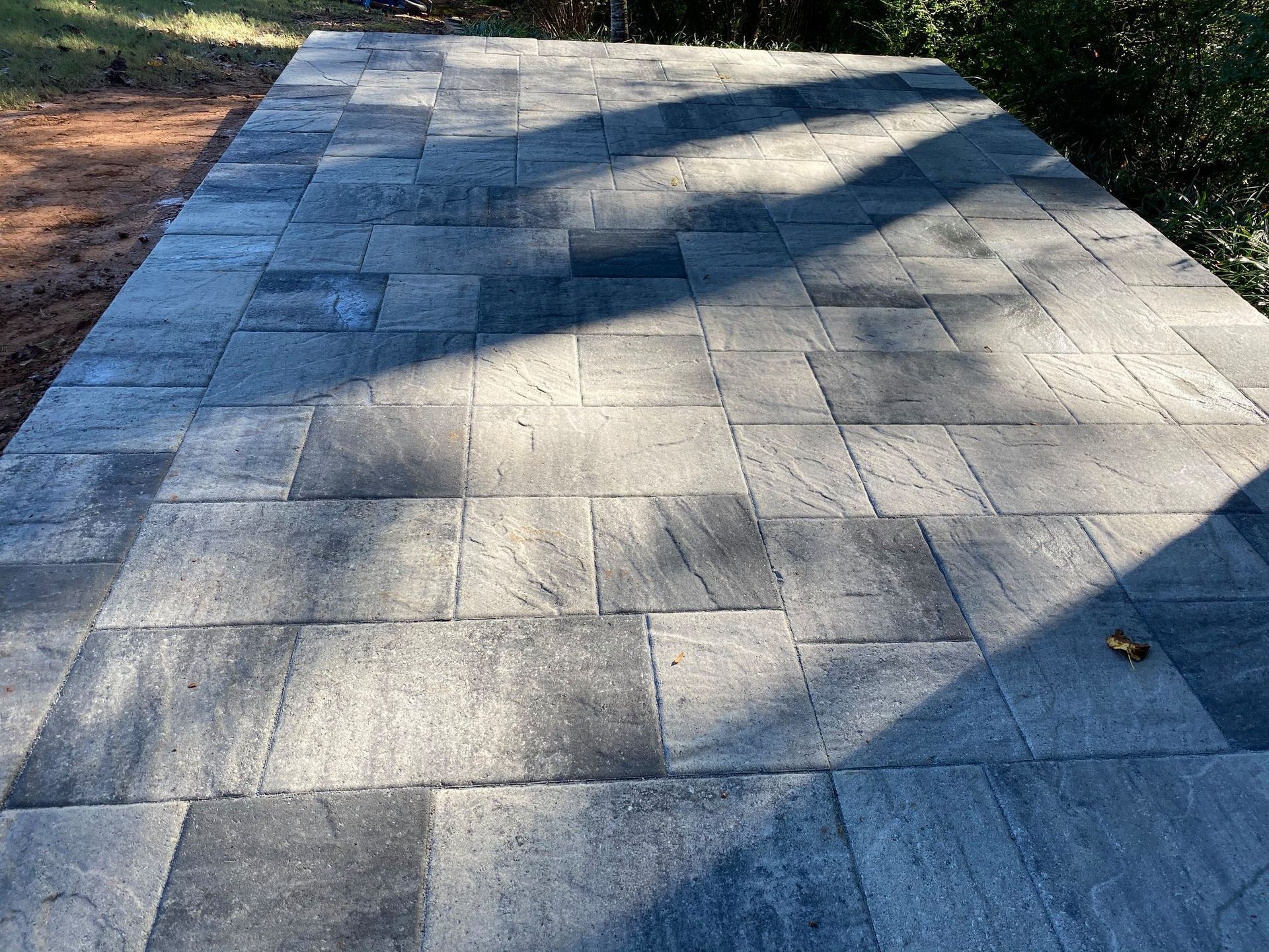 Sunlit stone pathway with diagonal shadows, bordered by grass and trees