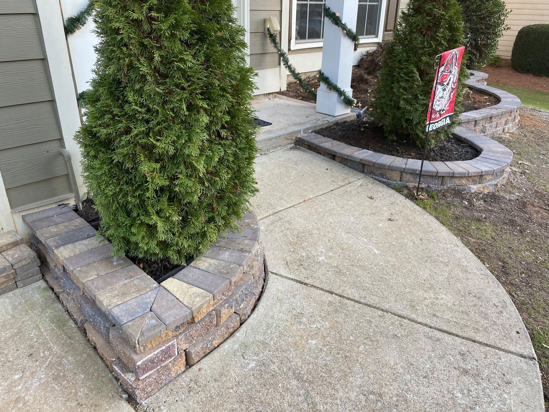 Curved concrete walkway beside brick planter with evergreen shrubs by a house entrance