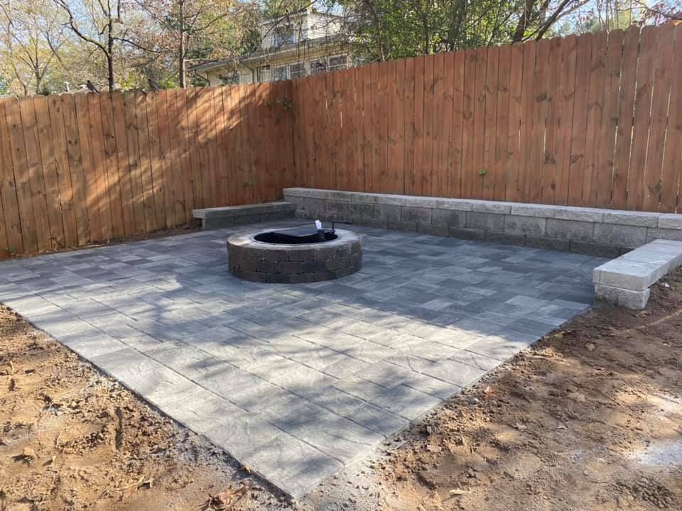 Backyard stone patio with a circular fire pit, wooden fence, and built-in benches.