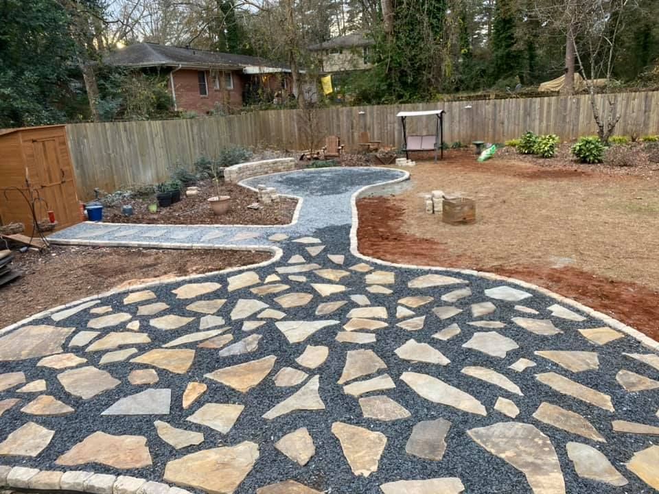 Backyard stone pathway with a curved blue-gray walkway and mosaic rock pattern, fenced by a wooden privacy fence.