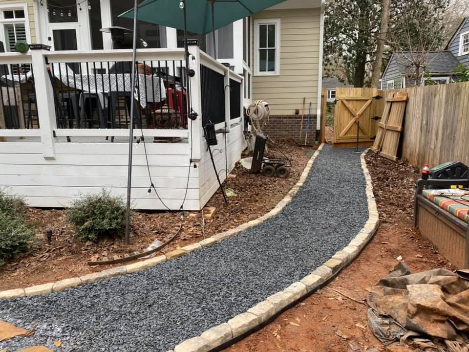 Gravel walkway beside a white porch and wooden fence, leading to a gate in a backyard