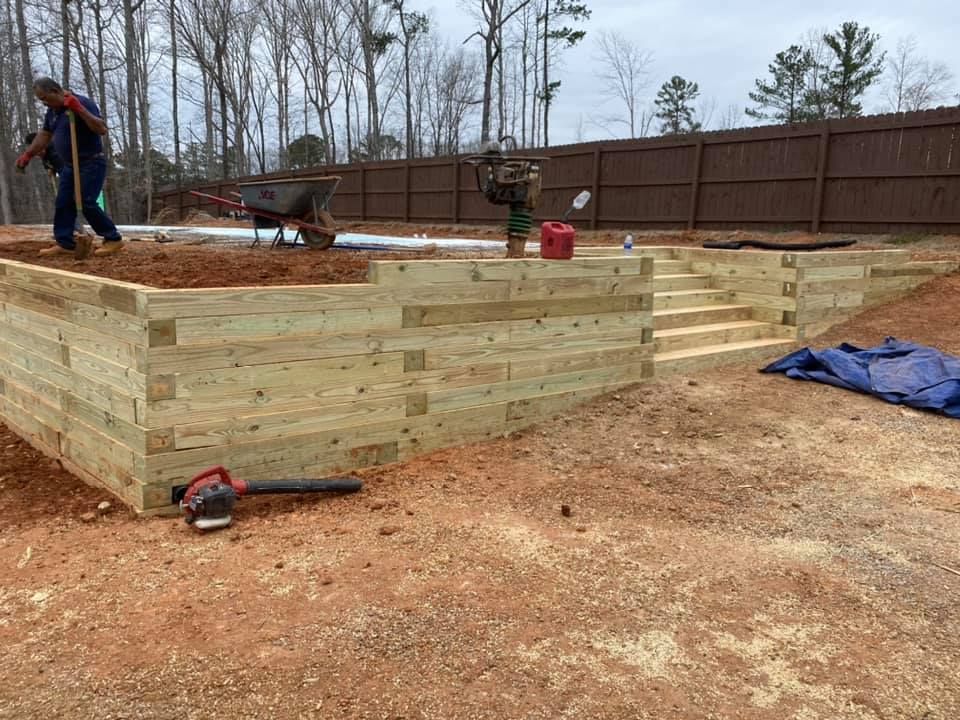 Person building a wood retaining wall at a construction site with tools and wheelbarrow