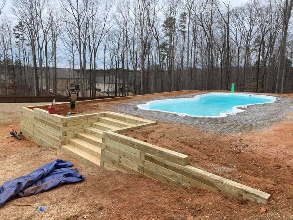 Backyard pool under construction with wooden retaining wall and gravel surround