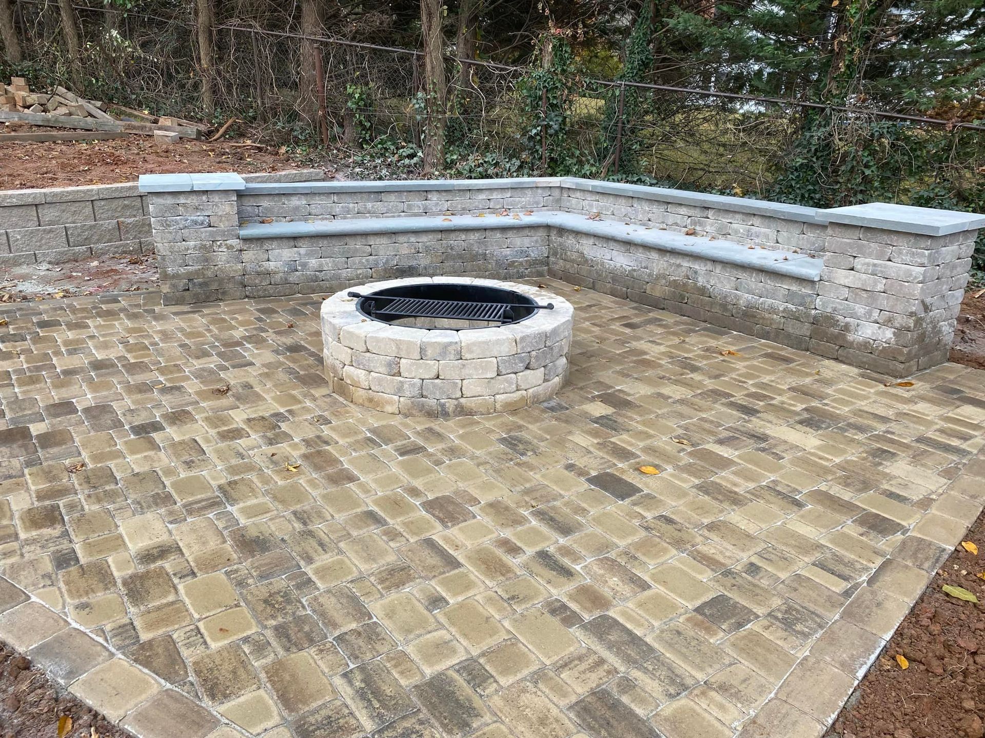 Stone patio with a circular fire pit and curved bench seating surrounded by trees