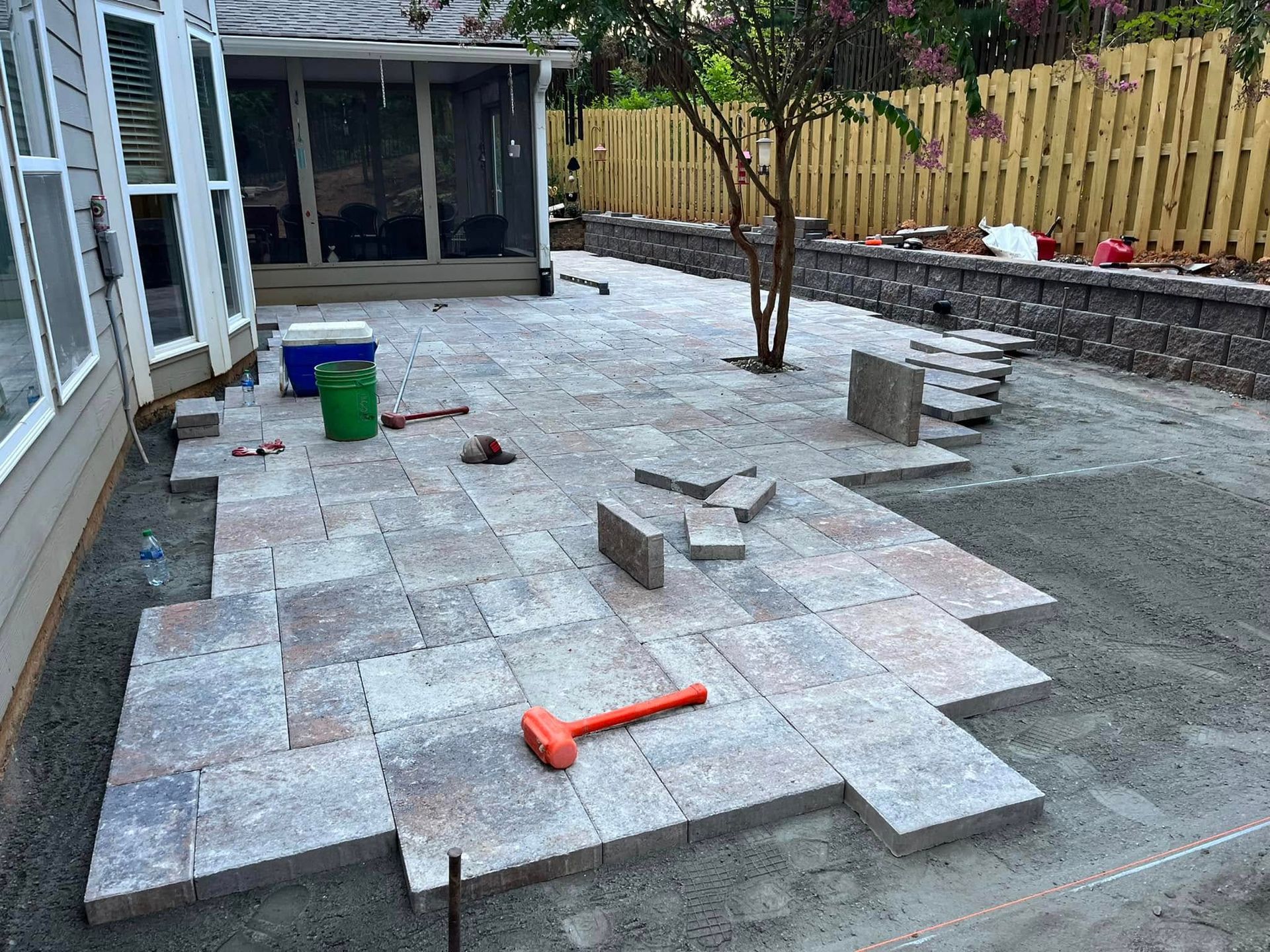 Patio under construction with gray pavers, tools, and a gravel border beside a house