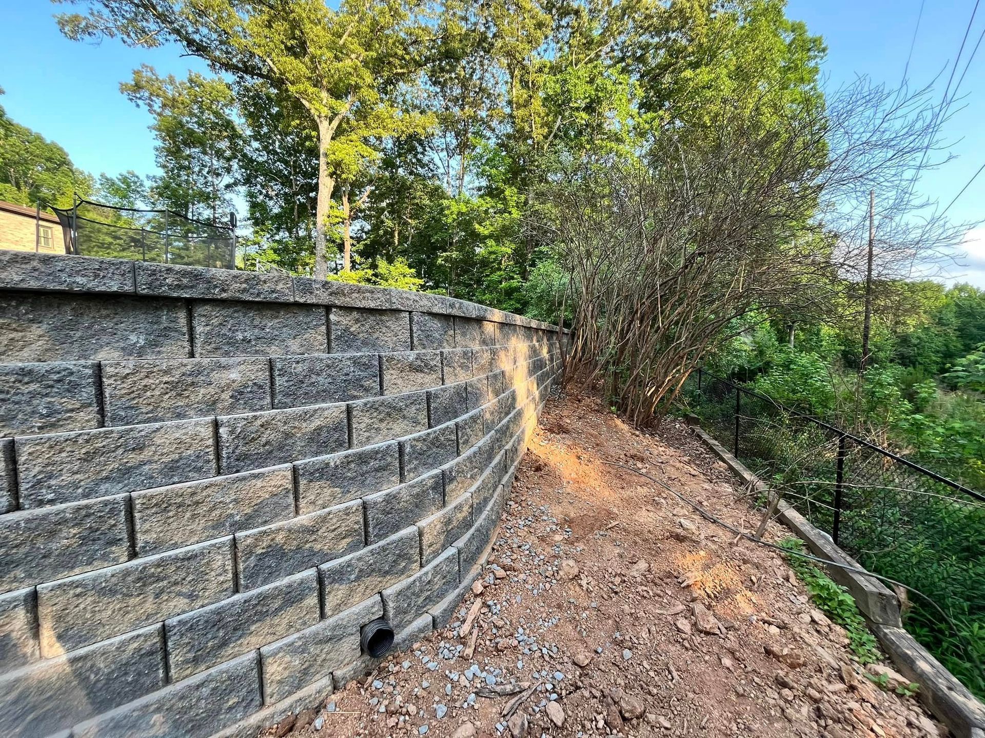 Curving stone retaining wall beside a dirt path on a wooded hillside