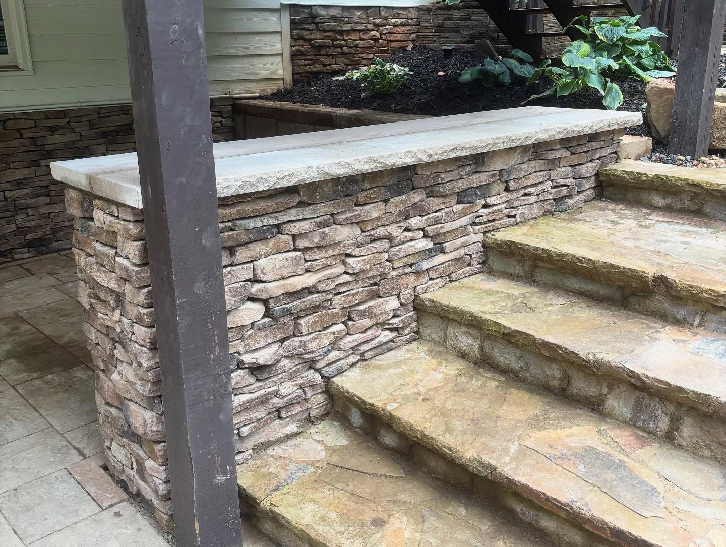 Stone steps beside a stacked-stone retaining wall and bench in an outdoor yard.