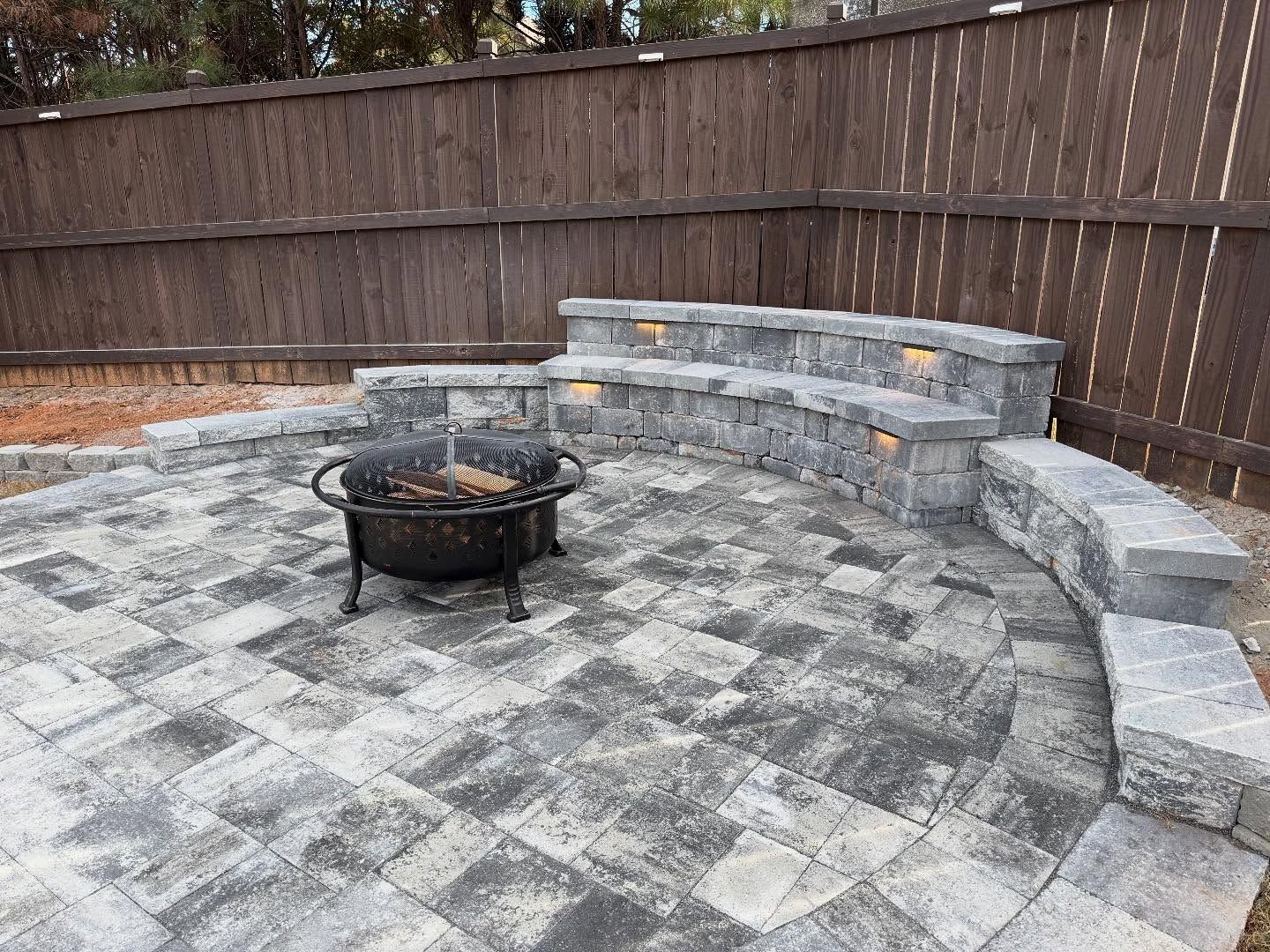 Stone patio with curved retaining wall and fire pit in a fenced backyard