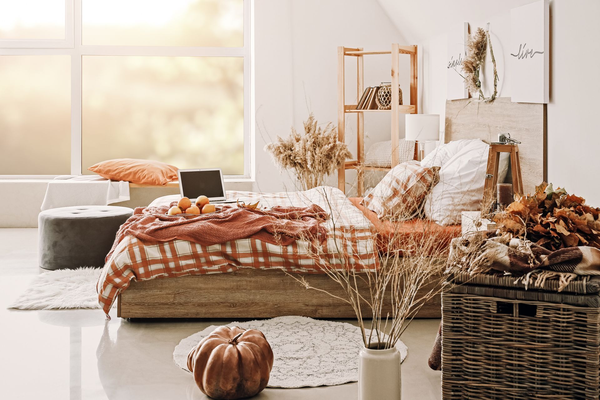 Cozy bedroom with autumn decor: bed with orange blanket, pumpkin, dried flowers, and a large window.