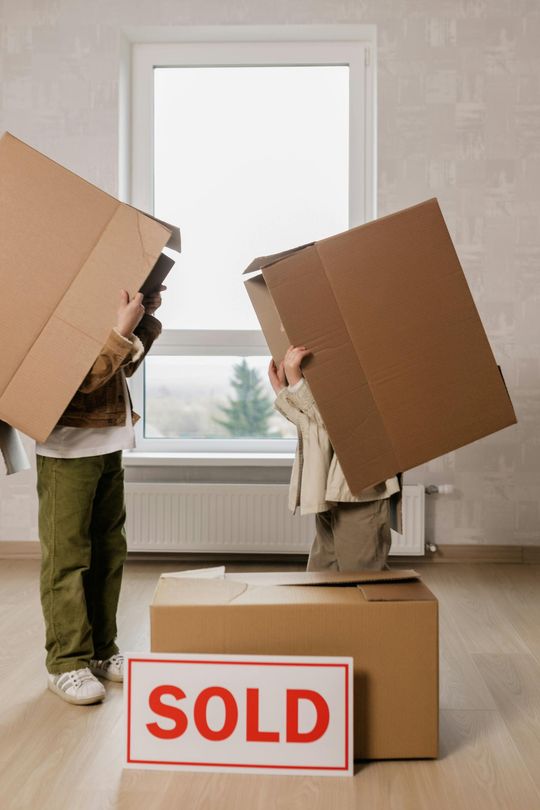 Two people carrying moving boxes in a bright room, with a red