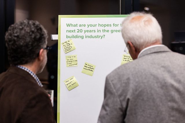 Two men are looking at a white board with sticky notes on it.