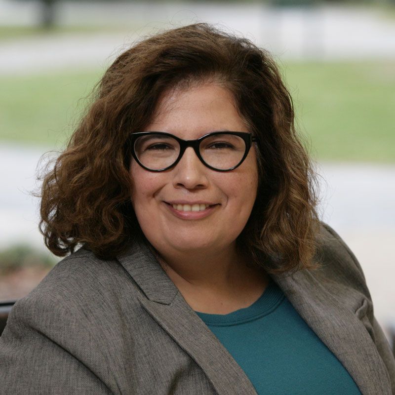A woman wearing glasses and a jacket is smiling for the camera.