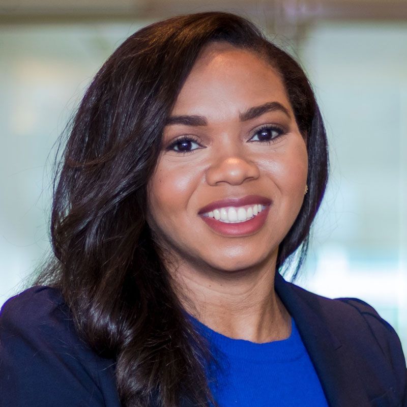 A woman wearing a blue shirt and a blue jacket is smiling for the camera.