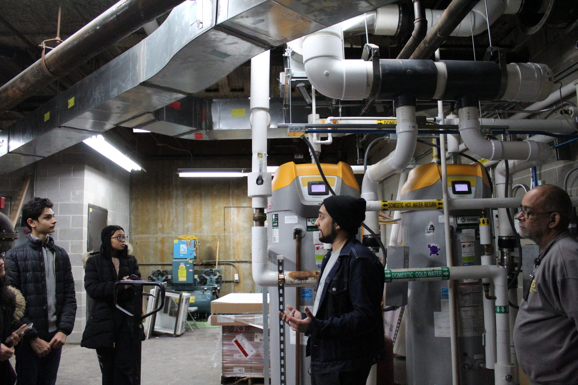 A group of people are listening to a mentor teach about boiler rooms.