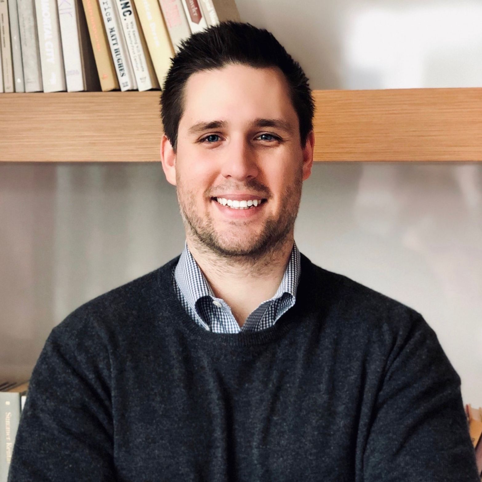 A man wearing a watch is smiling in front of a bookshelf