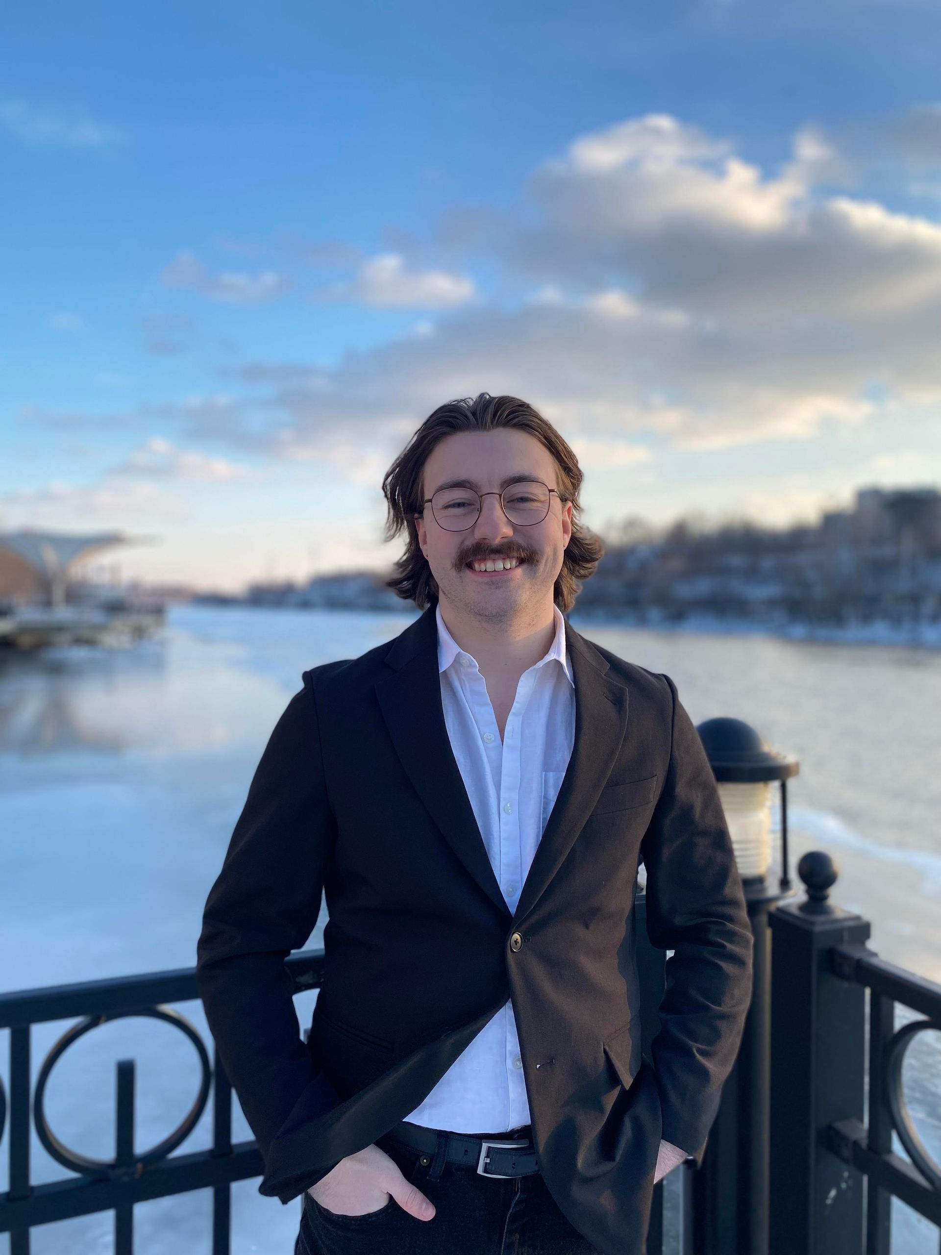 A man in a suit is standing next to a fence in front of a body of water.