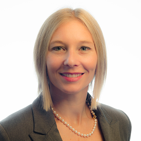 A woman wearing a pearl necklace and a suit jacket smiles for the camera