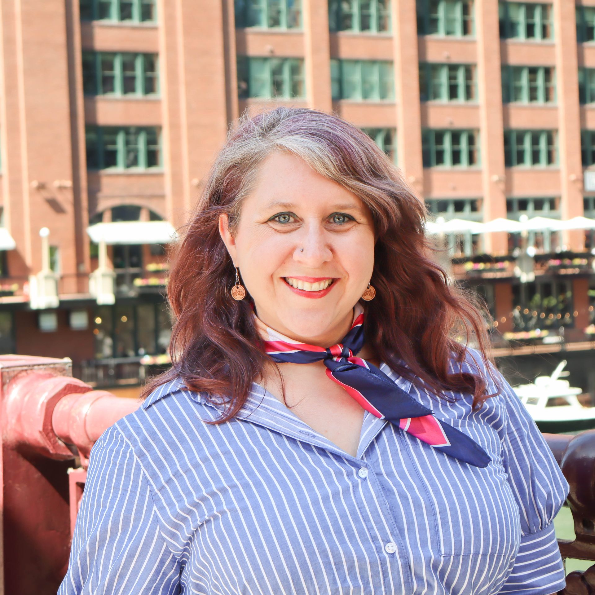 A woman wearing a striped shirt and a scarf smiles for the camera