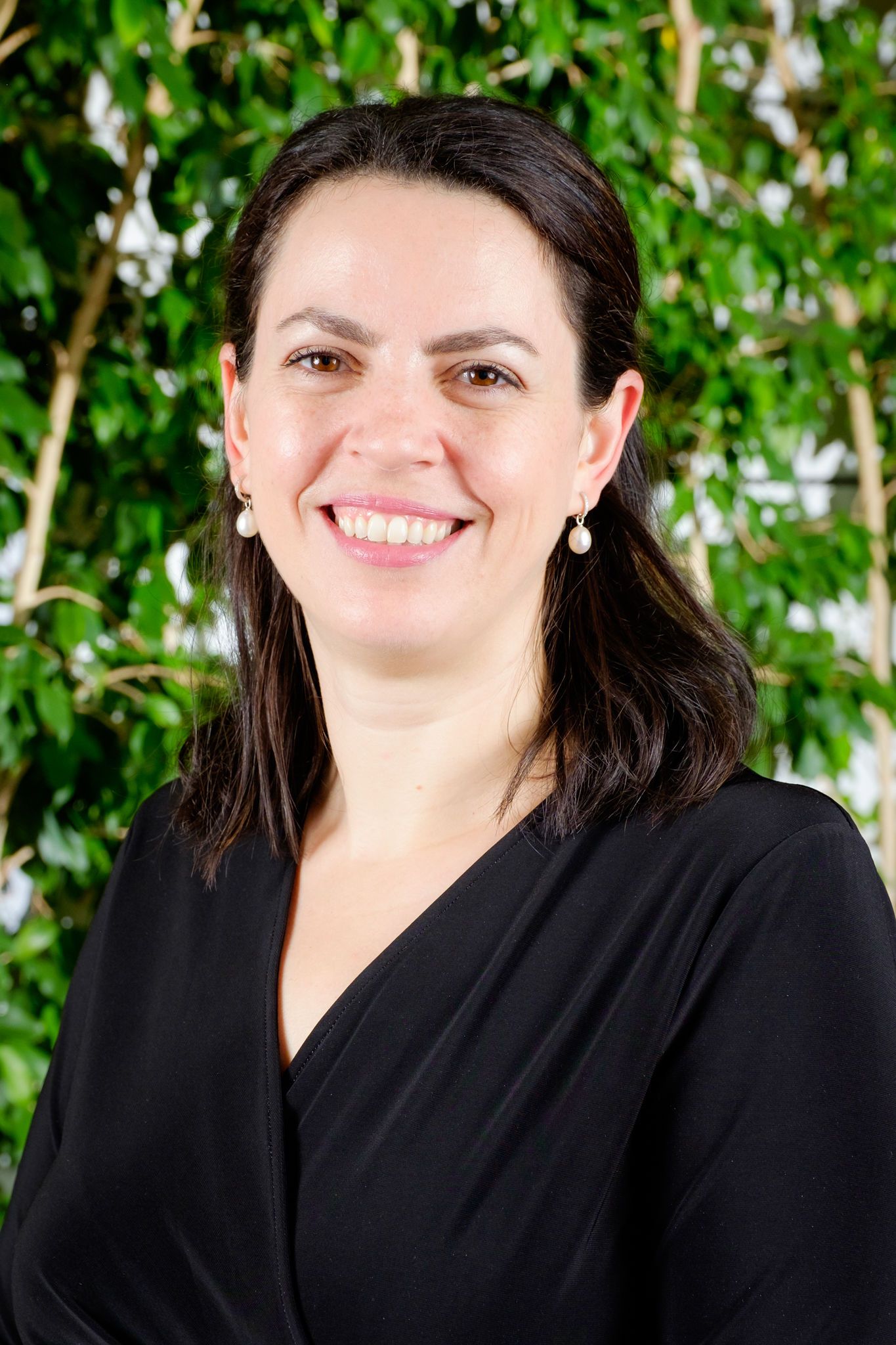 A woman in a black shirt is smiling in front of a tree.