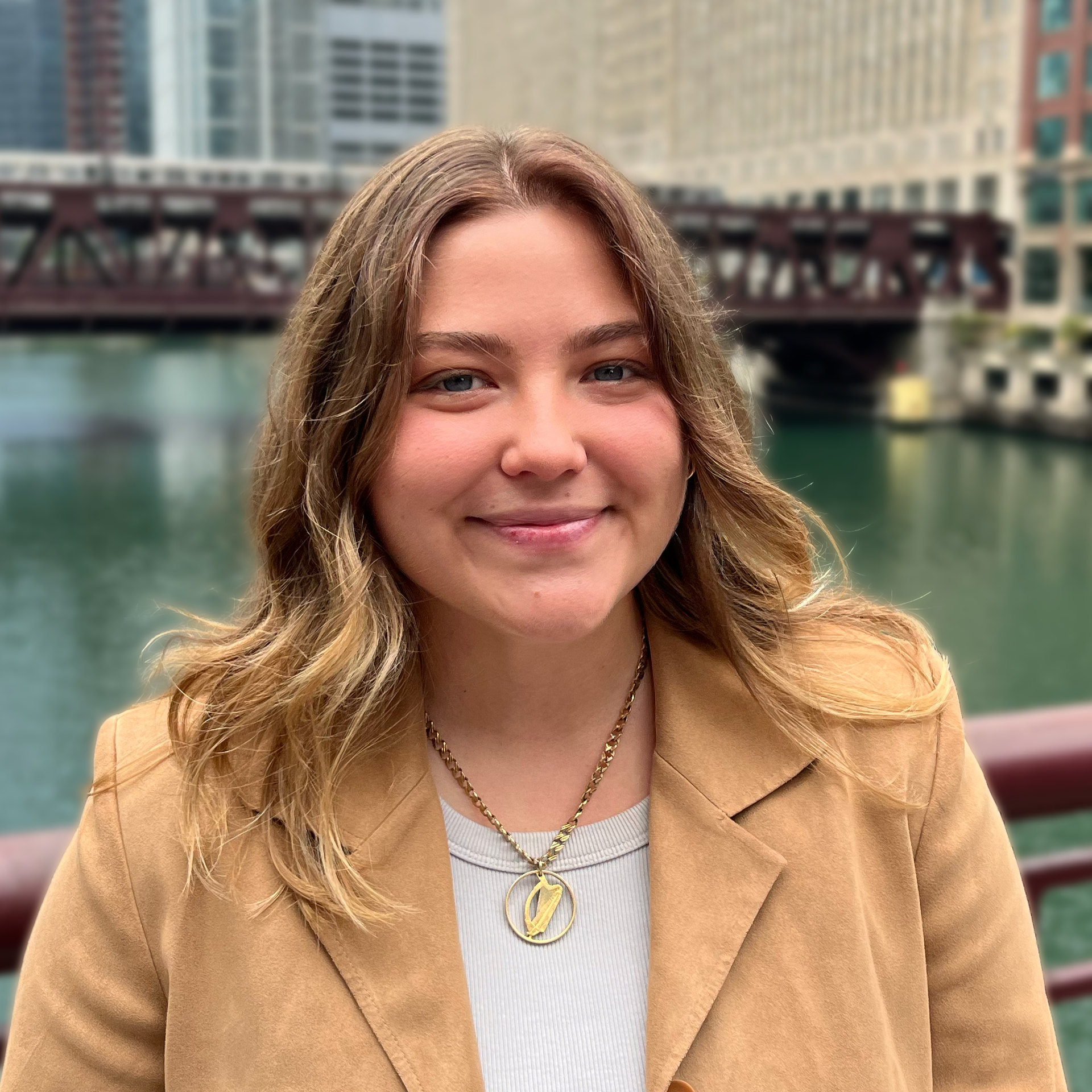 A woman wearing a tan jacket and a necklace is smiling for the camera.