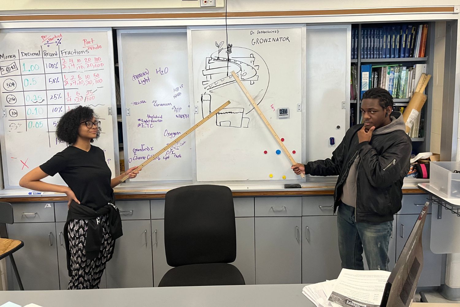A man and a woman are standing in front of a whiteboard in a classroom.