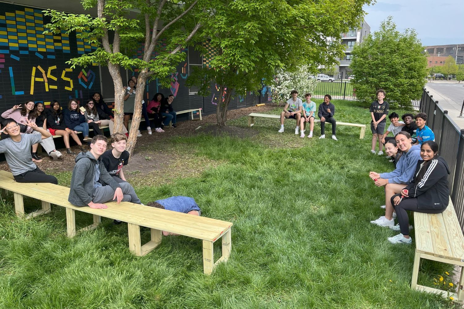 A group of people are sitting on wooden benches in the grass.